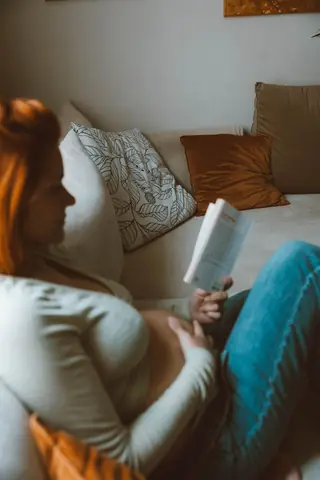 A pregnant woman reading a book on a cosy sofa